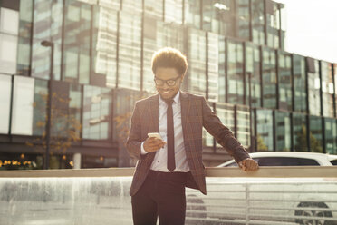 Smiling young businessman outdoors looking at cell phone - EBSF001093