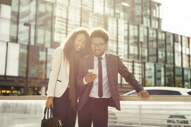 Two smiling young business people outdoors looking at smartphone - EBSF001094