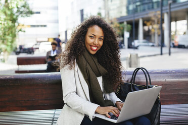 Lächelnde junge Frau mit Laptop auf einer Bank - EBSF001097