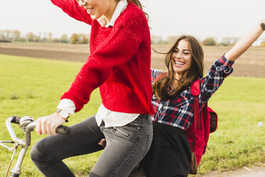 Two exuberant young women sharing a bicycle in rural landscape - UUF006039