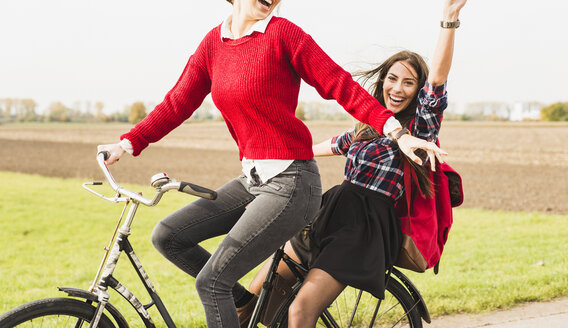 Zwei übermütige junge Frauen teilen sich ein Fahrrad in ländlicher Umgebung - UUF006041