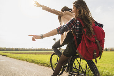 Zwei übermütige junge Frauen teilen sich ein Fahrrad in ländlicher Umgebung - UUF006045