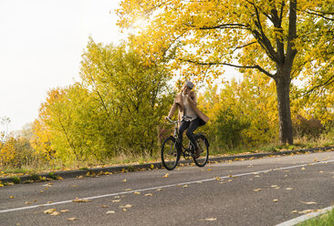 Junge Frau mit Handy auf dem Fahrrad in einer Herbstlandschaft - UUF006048