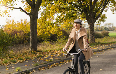 Young woman riding bicycle in autumn landscape - UUF006049