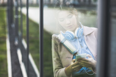 Young woman leaning at glass front looking on cell phone - UUF006076