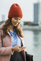 Junge Frau am Flussufer schaut auf ihr Handy - UUF006081