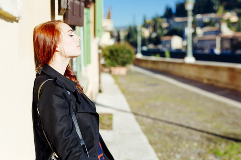 Italien, Verona, junge Frau lehnt an Hauswand im Sonnenlicht, lizenzfreies Stockfoto