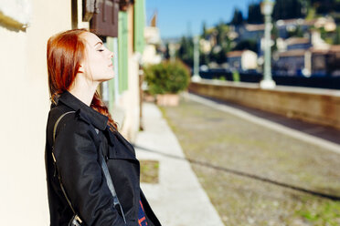 Italy, Verona, young woman leaning against house wall in sunlight - GIOF000530