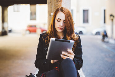 Junge Frau schaut auf ein digitales Tablet im Freien - GIOF000535
