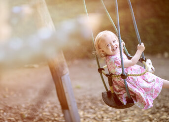 Portrait of blond little girl wearing dress with floral design sitting on a swing - NIF000051