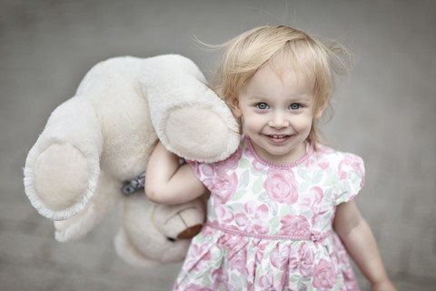 Porträt eines lächelnden blonden kleinen Mädchens mit ihrem Teddybär, lizenzfreies Stockfoto