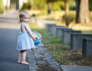 Barfußes blondes kleines Mädchen steht mit ihrem Ball am Straßenrand - NIF000063