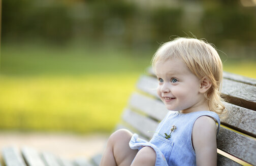 Porträt eines lächelnden blonden kleinen Mädchens, das auf einer Parkbank sitzt - NIF000065