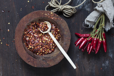 Bunch of red chili peppers, cord and plate of chili flakes on wood - SBDF002411