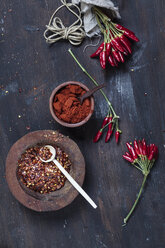 Bunches of red chili peppers, cord plate of chili flakes and bowl with chili powder on wood - SBDF002412