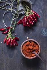 Bunches of red chili peppers and bowl with chili powder on wood - SBDF002413