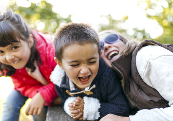 Drei lachende Kinder spielen zusammen in einem Park - MGOF001058