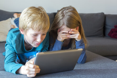 Junge und Mädchen liegen auf der Couch und benutzen ein digitales Tablet - SARF002311