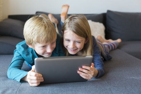 Junge und Mädchen liegen nebeneinander auf der Couch und benutzen ein digitales Tablet - SARF002312