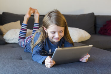 Smiling girl lying on the couch using digital tablet - SARF002313