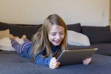 Lächelndes Mädchen auf der Couch liegend mit digitalem Tablet - SARF002314