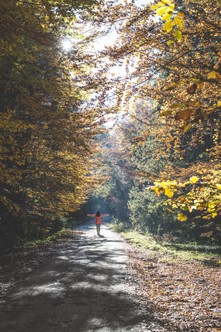 Rückenansicht einer Frau, die das Sonnenlicht in einem herbstlichen Wald genießt, lizenzfreies Stockfoto