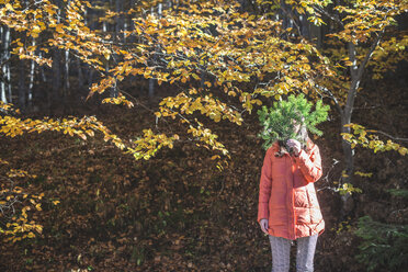Frau versteckt ihr Gesicht hinter einem Tannenzweig im herbstlichen Wald - DEGF000586