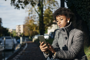 Schöne schwarze Frau mit Smartphone, draußen im Herbst - MAUF000012
