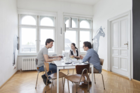 Unscharfe Ansicht von drei kreativen Geschäftsleuten bei einer Besprechung in einem modernen Büro, lizenzfreies Stockfoto