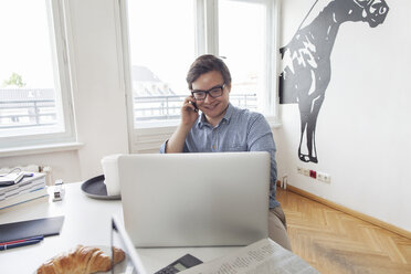 Smiling young businesssman with laptop and cell phone in a modern office - JUBF000062