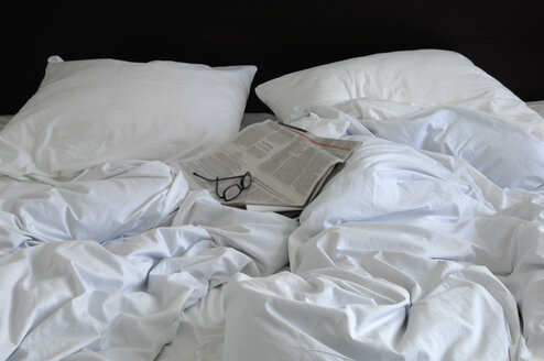 Rumpled bed with glasses and newspaper - ASF005757