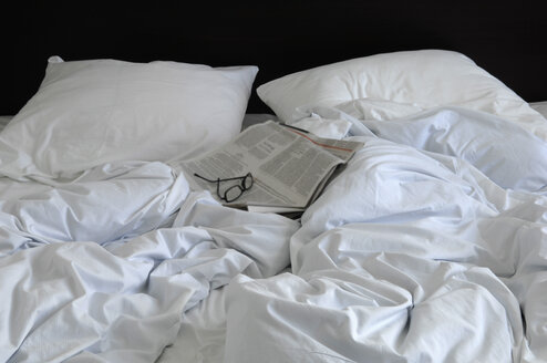 Zerknittertes Bett mit Gläsern und Zeitung - ASF005757