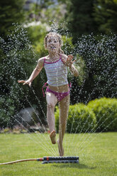 Girl jumping over sprinkler in garden - PAF001466