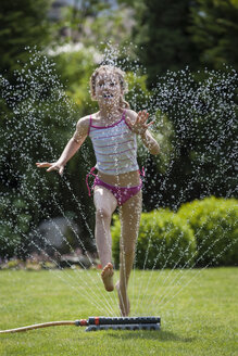 Mädchen springt über Sprinkler im Garten - PAF001466