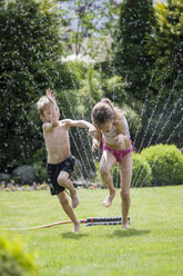 Children jumping over sprinkler in garden - PAF001468