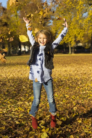 Glückliches kleines Mädchen, das Herbstblätter wirft und dabei in die Luft springt, lizenzfreies Stockfoto