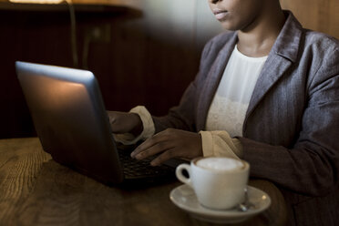 Junge Frau sitzt in einem Café und arbeitet mit einem Laptop - MAUF000018