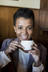 Porträt einer lächelnden jungen Frau, die mit einer Tasse Kaffee in einem Café sitzt - MAUF000022