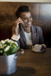 Portrait of smiling young woman sitting in a cafe telephoning with smartphone - MAUF000029
