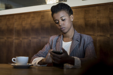 Porträt einer jungen Frau, die in einem Café sitzt und ihr Smartphone benutzt - MAUF000030