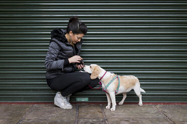 Woman and her dog on a sidewalk in front of a roller shutter - MAUF000038
