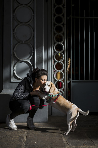 UK, London, Frau knuddelt ihren Hund auf dem Gehweg vor einem Haus, lizenzfreies Stockfoto