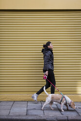 Woman and her dog walking on pavement in front of a roller shutter - MAUF000040