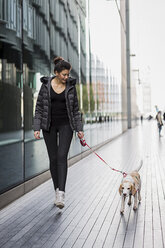 UK, London, woman and her dog walking on pavement in the city - MAUF000051