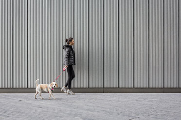 Woman and her dog walking on pavement in front of a metal facade - MAUF000052