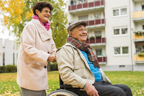 Ältere Frau schiebt ihren Mann im Rollstuhl, lizenzfreies Stockfoto