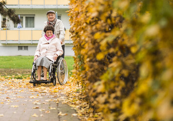 Senior man pushing wife in wheelchair - UUF006114