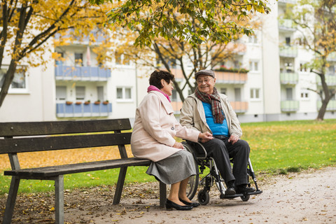 Ältere Frau sitzt auf einer Bank neben ihrem Mann im Rollstuhl, lizenzfreies Stockfoto