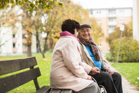 Senior man in wheelchair holding hands with wife on bench - UUF006117