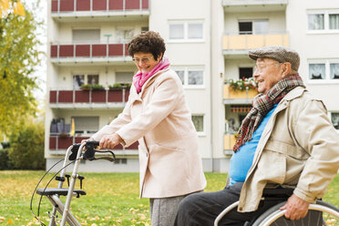 Senior woman with wheeled walker and senior man in wheelchair outdoors in autumn - UUF006124